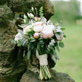 bukiet ślubny oparty o skałę. bogaty bukiet ślubny z białych i różowych piwonii, z goździkami i eukaliptusem