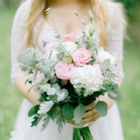 panna młoda trzyma przed sobą bukiet ślubny z różowymi pełnikami i z eukaliptusem oraz z białymi goździkami