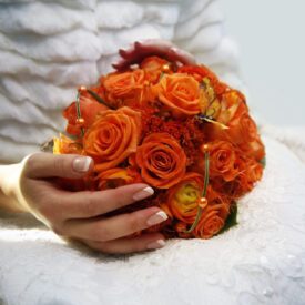 panna młoda trzyma na kolanach bukiet ślubny z pomarańczowych róż
