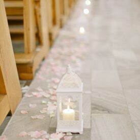 przystrojenie kościoła na ślub, biały lampion z zapaloną świeczką a wokół rozsypane różowe płatki kwiatów